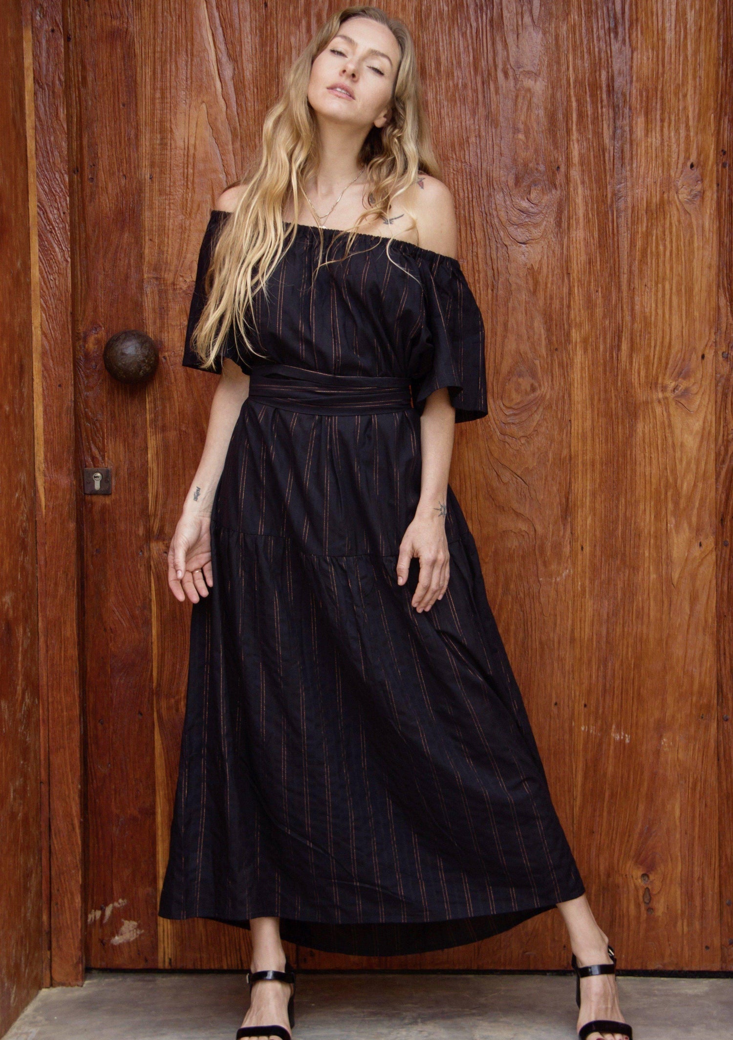 ADÈLE DRESS • Soft cotton maxi length dress featuring off-shoulder neckline, wrap-around belt, and side pockets in black with contrast fine copper fleck stripes. Available in one size.