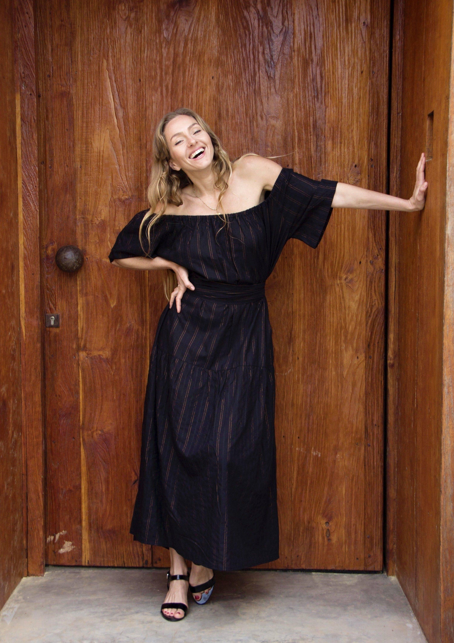 ADÈLE DRESS • Soft cotton maxi length dress featuring off-shoulder neckline, wrap-around belt, and side pockets in black with contrast fine copper fleck stripes. Available in one size.